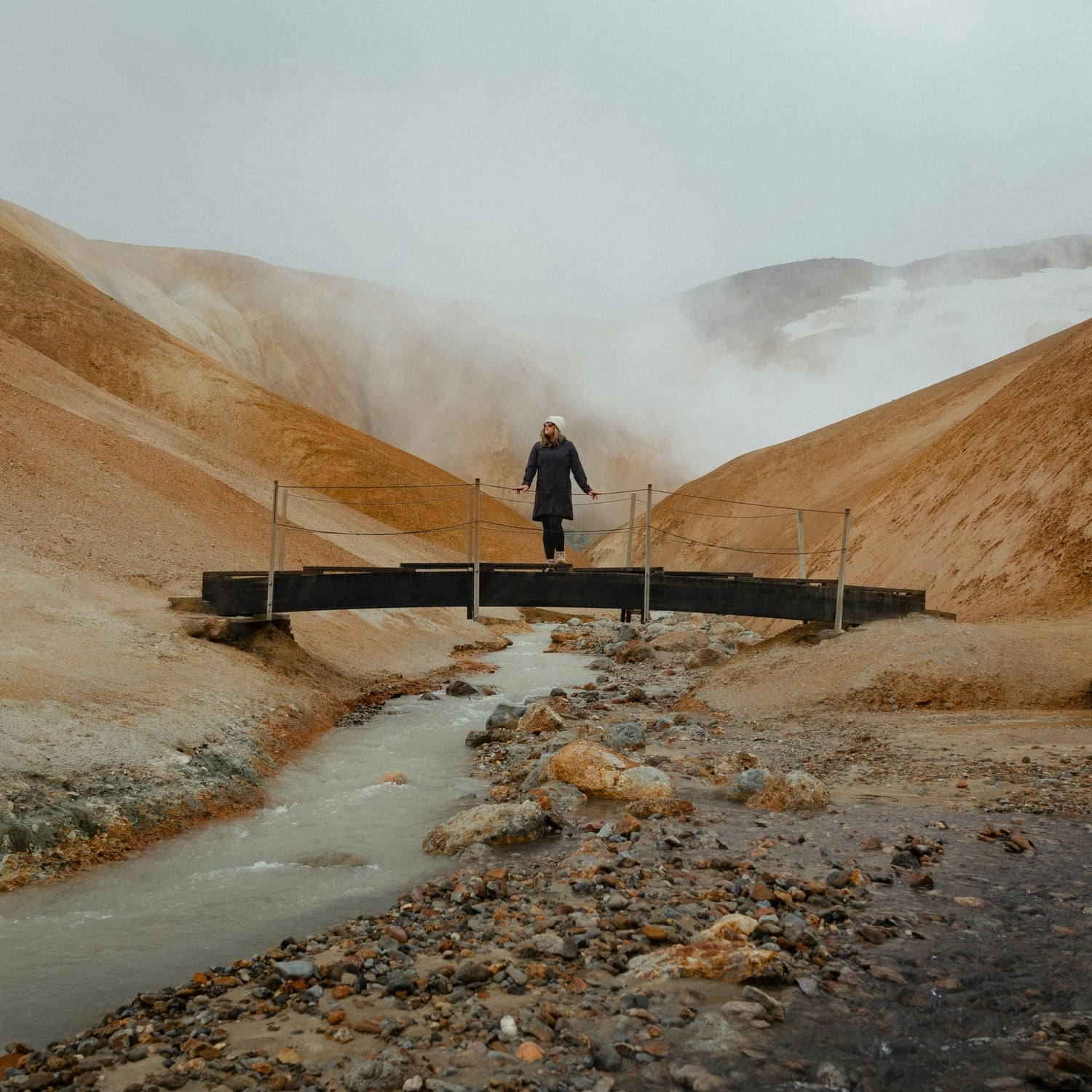 Woman standing on bridge over stream in the mountains.